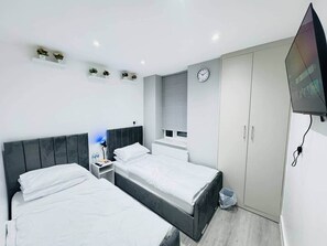 Un dormitorio moderno con dos camas, una mesita de noche, un televisor y un armario.