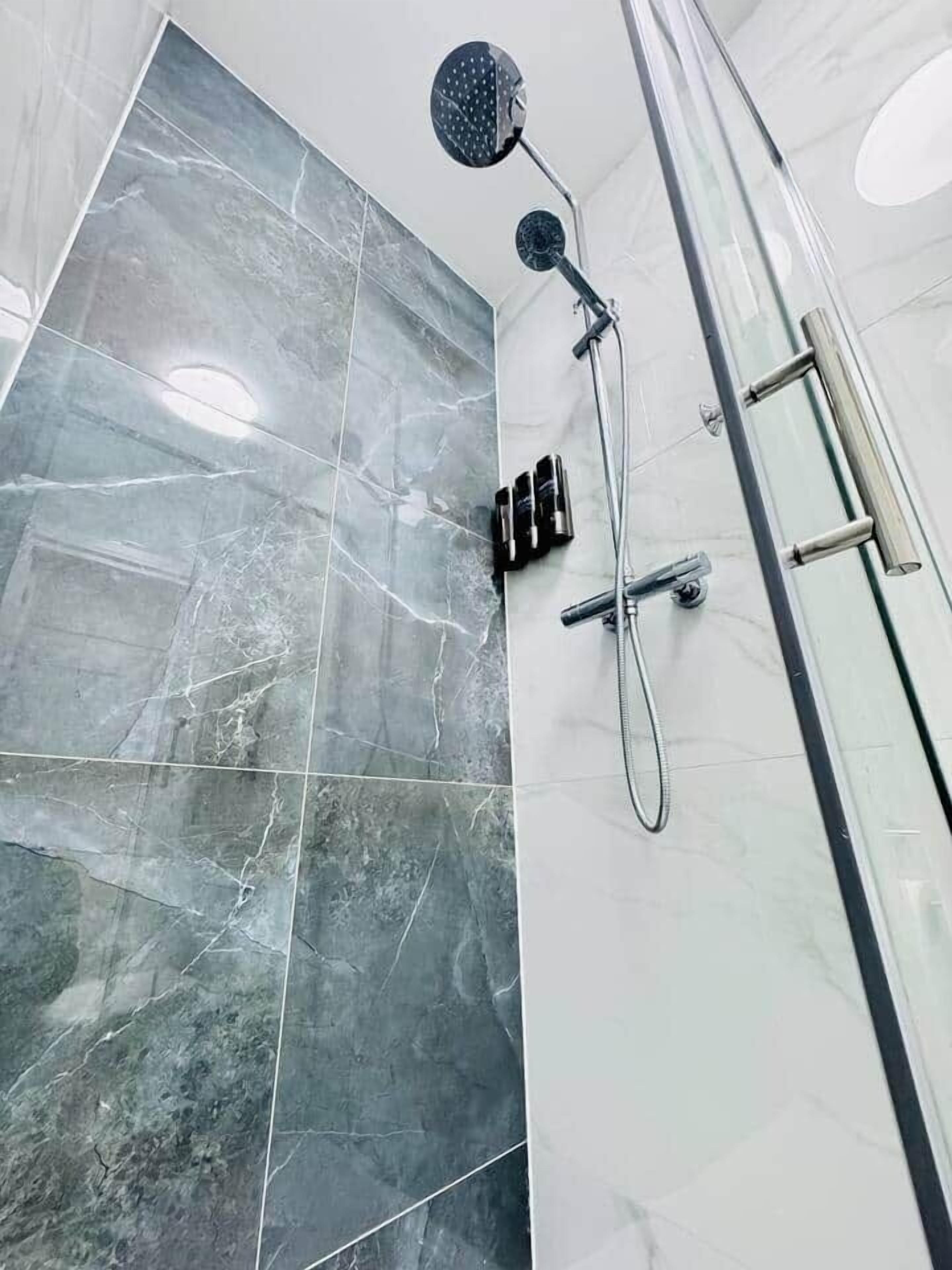 Un baño con ducha, puerta de cristal y pared de mármol.