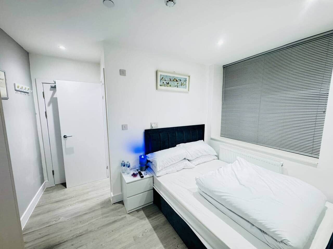 Un dormitorio con cama, mesita de noche y ventana con persianas.