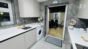 A modern kitchen with a built-in washing machine, a sink, and a dining area visible through a glass door. - Private En-Suite Room near Cardiff City Centre (Cardiff)