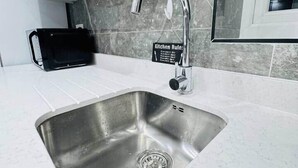 A modern kitchen with a stainless steel sink, a black microwave, and a marble backsplash. - Private En-Suite Room near Cardiff City Centre (Cardiff)