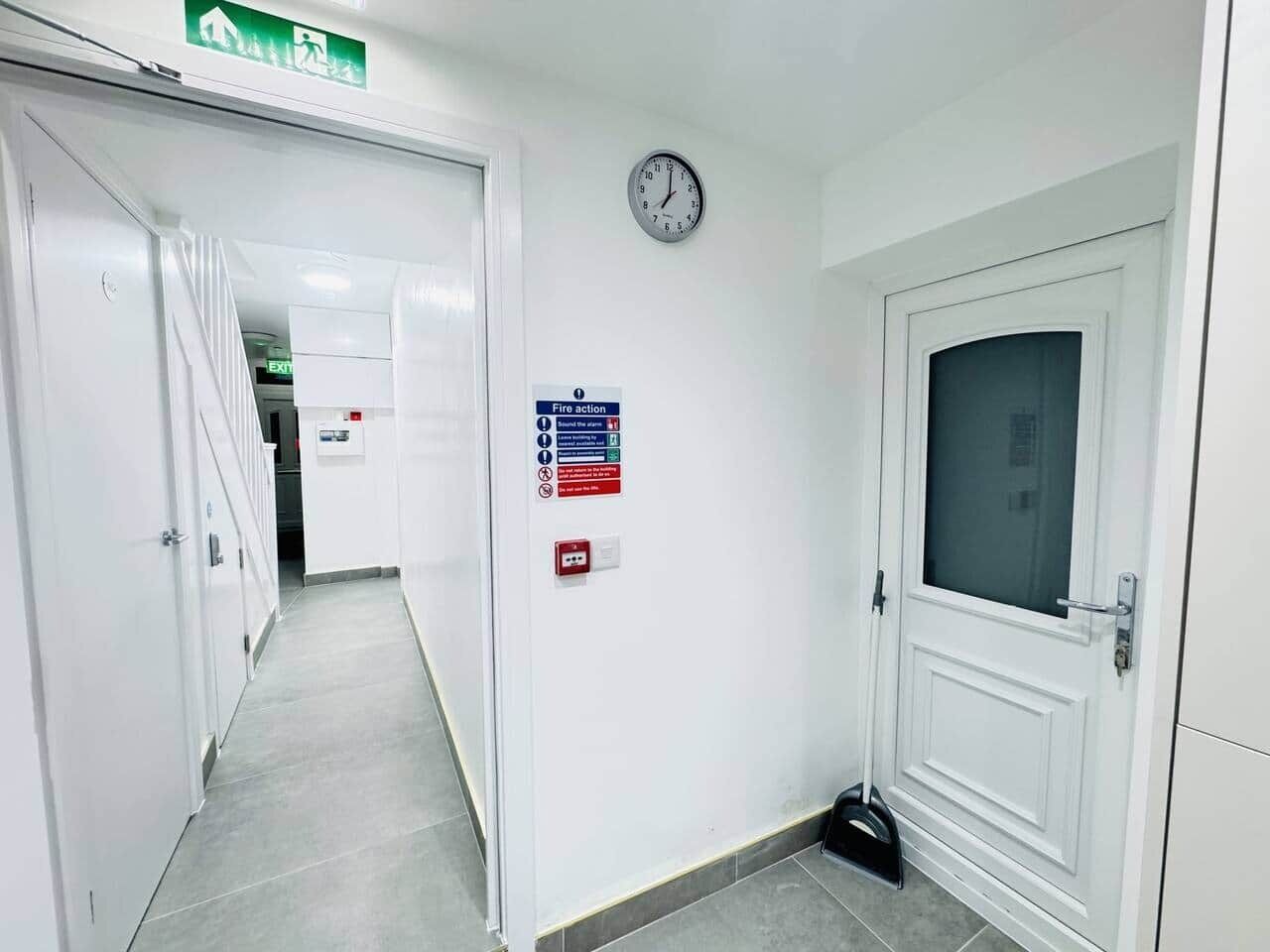 A hallway with white walls, a clock, a fire action sign, and an exit sign.