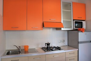 A kitchen with orange cabinets, a white microwave, and a stainless steel refrigerator. - Lovely Flat With Patio (San Michele al Tagliamento)