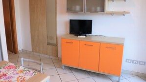 A room with a wooden door, a cabinet with a television on top, and a tiled floor. - Lovely Flat With Patio (San Michele al Tagliamento)