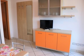 Um quarto com porta de madeira, um armário com uma televisão por cima e chão de azulejos.