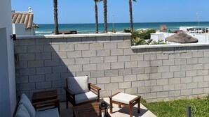 A patio area with a view of the ocean, featuring a brick wall, wooden furniture, and a thatched roof. - Agoodplan Playa El Palmar de Vejer (Vejer de la Frontera)