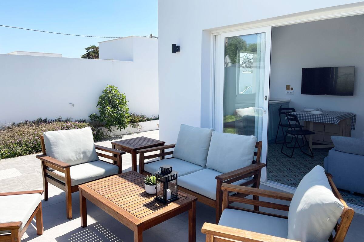 Un patio con sofá, sillas, mesa y una pequeña cocina con televisión.