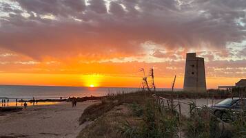 Ein Strand mit einem Turm, Sanddünen und einem Sonnenuntergang.