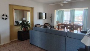 Una sala de estar con sofá, una mesa de comedor con sillas, televisión y ventana con cortinas.