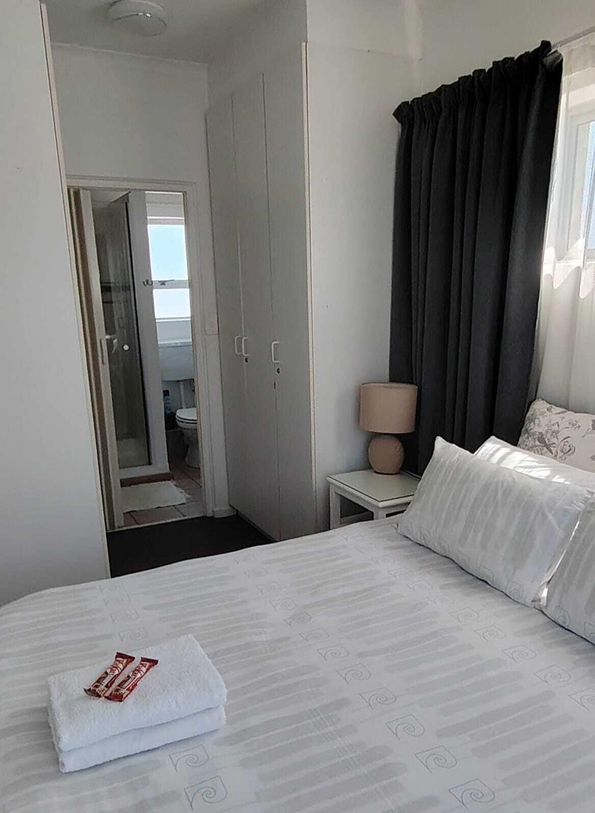 Habitación de hotel con cama, mesita de noche, lámpara y vista al baño.
