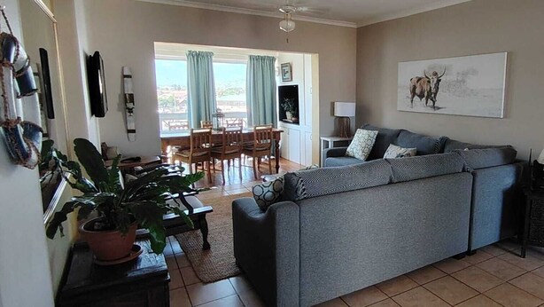 Una sala de estar con un sofá gris, una mesa de comedor con sillas, un televisor y un ventanal con cortinas.