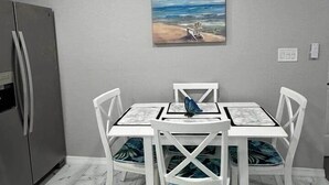 En matplats med ett bord och stolar, en tavla på väggen och ett kylskåp.