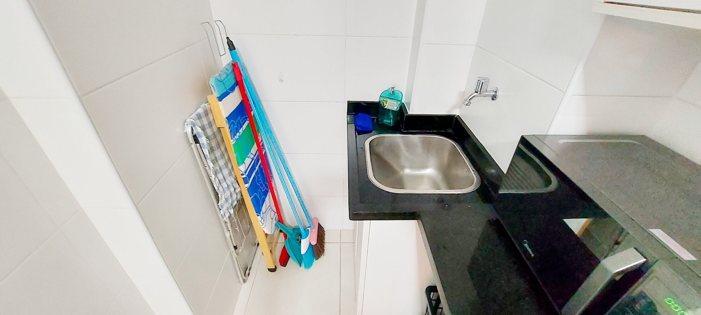 A small kitchen with a sink, a drying rack, and a few cleaning supplies.