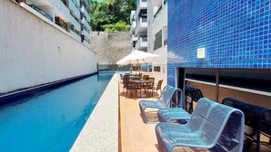 Una piscina con lettini e un tavolo, circondata da un muro bianco e un edificio con piastrelle blu.