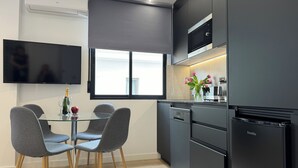 Una cocina moderna con microondas, estufa y refrigerador integrados, una mesa de comedor de vidrio con sillas, y un ventanal que proporciona luz natural.