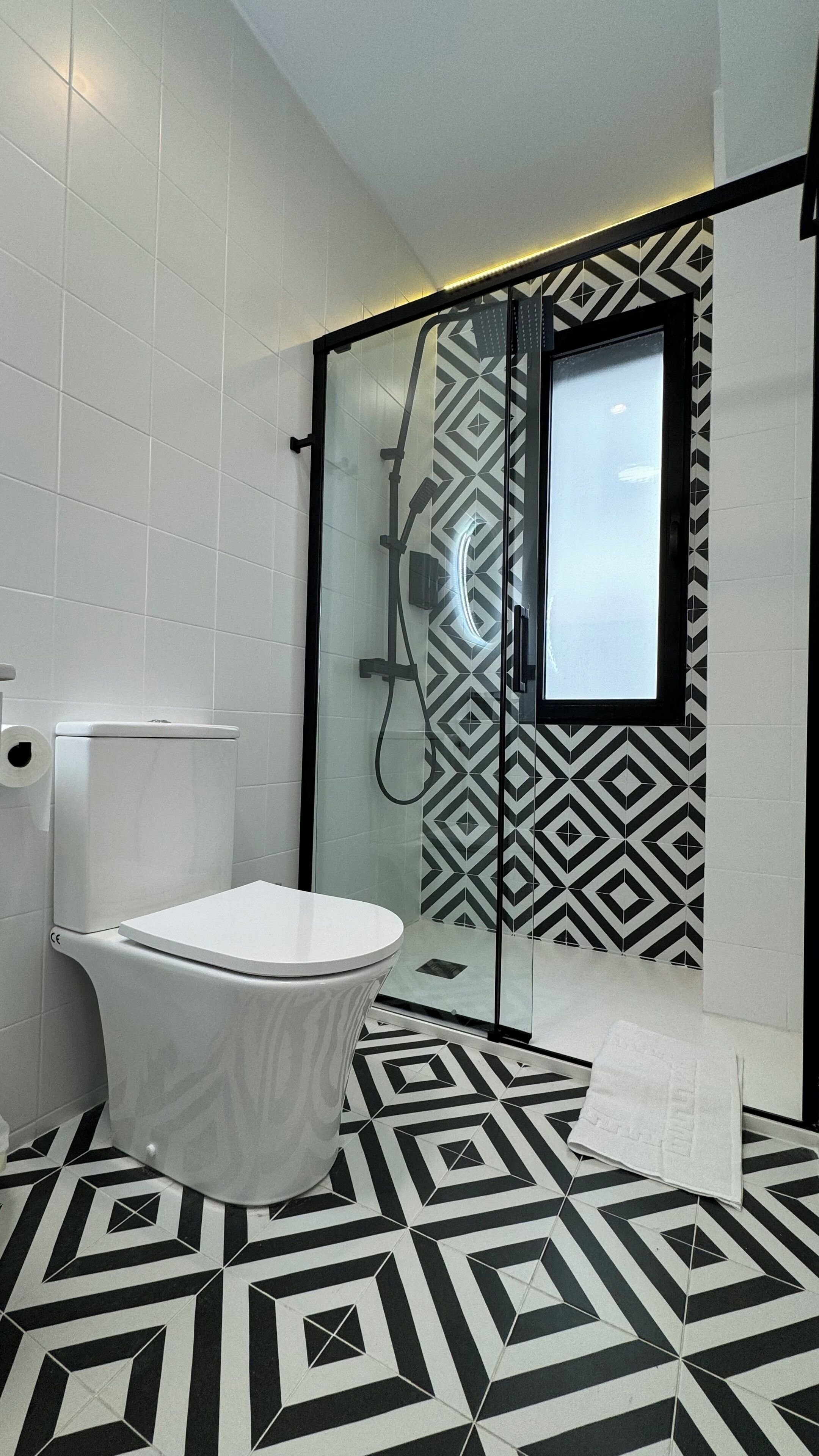 A modern bathroom with a freestanding toilet, a glass shower enclosure, and a geometric patterned floor.