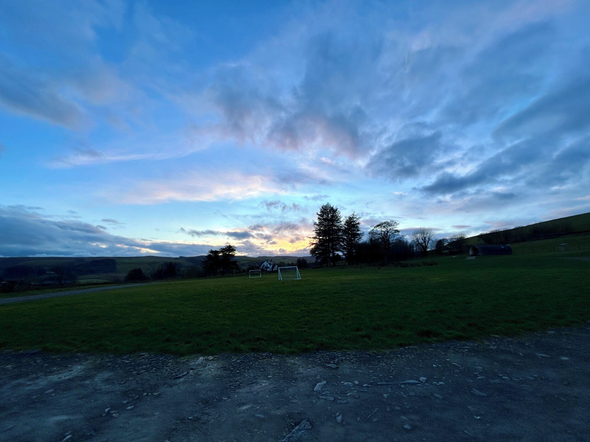 A rural landscape with a dirt road, grassy field, and a white building in the distance.
