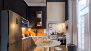 A modern kitchen with a stainless steel refrigerator, wooden cabinets, a round dining table with stools, and a window providing natural light. - Apartment 'Victorian Beach House Luisa Todi' with Balcony and Wi-Fi (Setúbal)