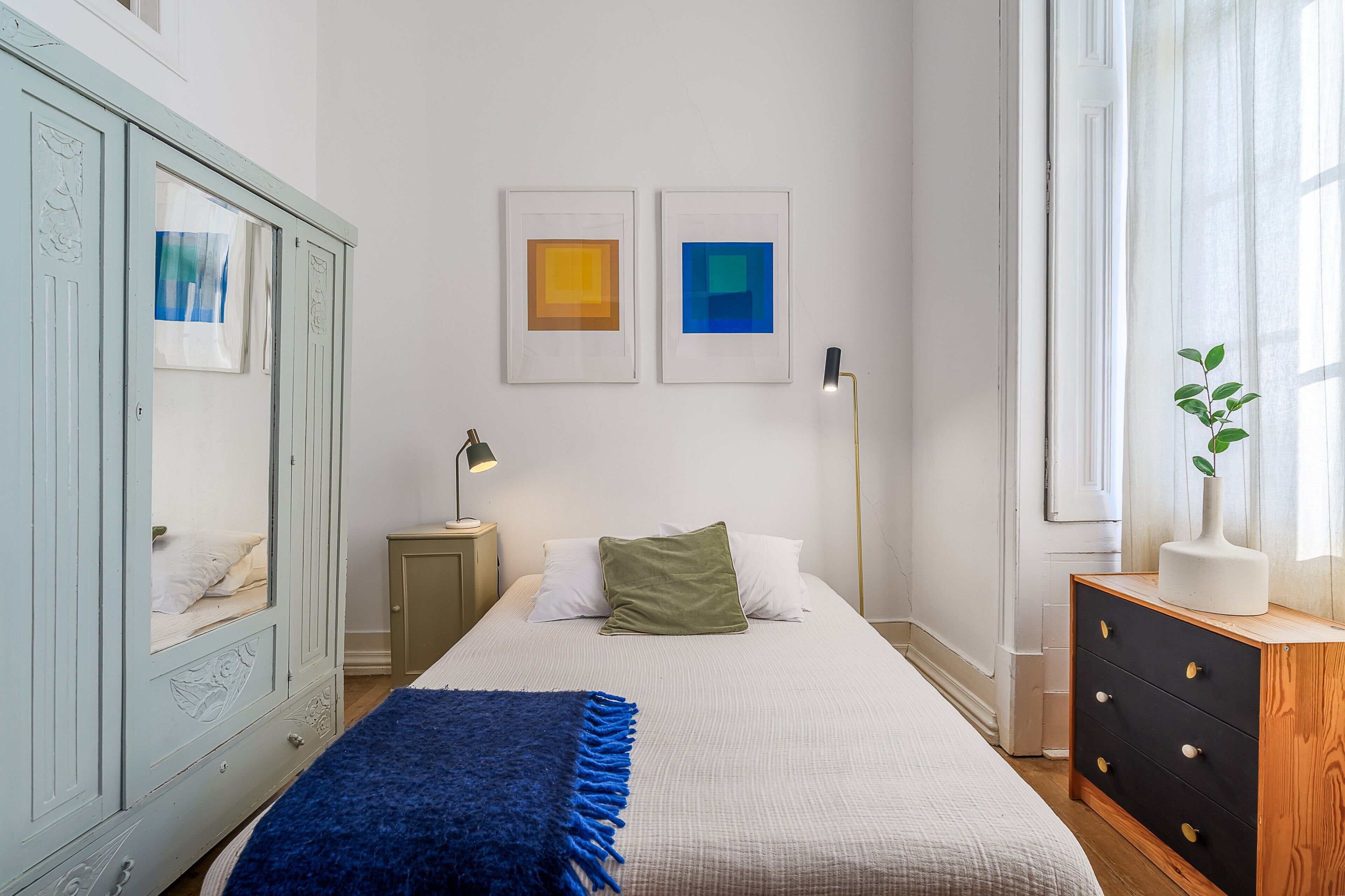 Quarto com cama, duas obras de arte emolduradas, abajur, cômoda e uma planta.
