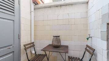 Um pequeno quarto com piso de azulejos, uma mesa e duas cadeiras, um vaso de planta e uma janela.