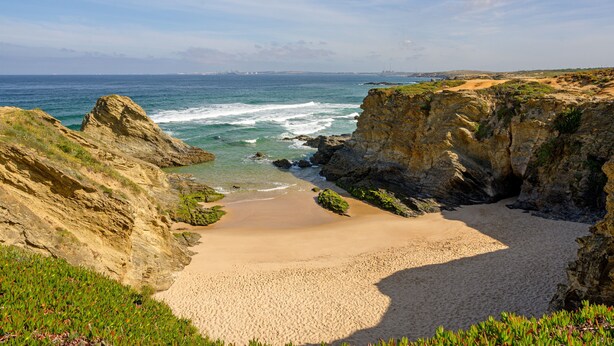 Une plage côtière bordée de falaises rocheuses et d’une étendue de sable.