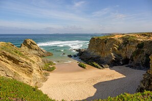 Une plage côtière bordée de falaises rocheuses et d’une étendue de sable.