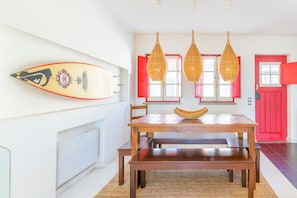 Un comedor con una mesa de madera, lámparas colgantes de mimbre y una decoración con una tabla de surf.