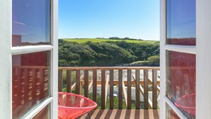 Un balcon donnant sur un paysage verdoyant, avec une chaise rouge et une terrasse en bois.