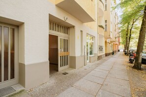 A residential building with a paved sidewalk, a gated entrance, and parked cars along the street. - Boutique Urban Nest | Cozy & Central 1 (Berlin)