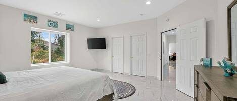 A modern bedroom with a large bed, a TV mounted on the wall, and a view of the outdoors through a window.