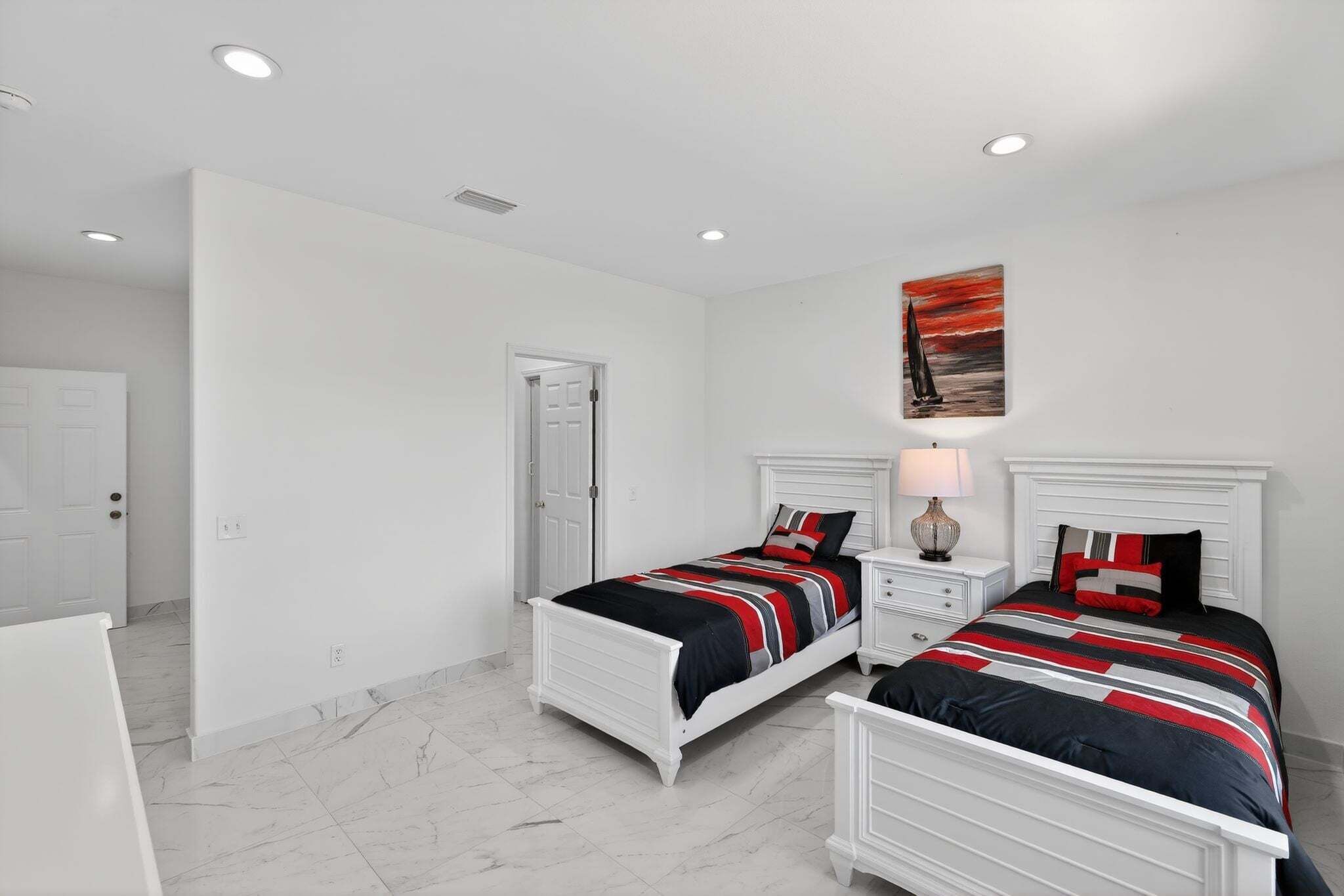A bedroom with two beds, white headboards, and a painting on the wall.
