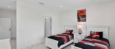 A bedroom with two beds, white headboards, and a painting on the wall.