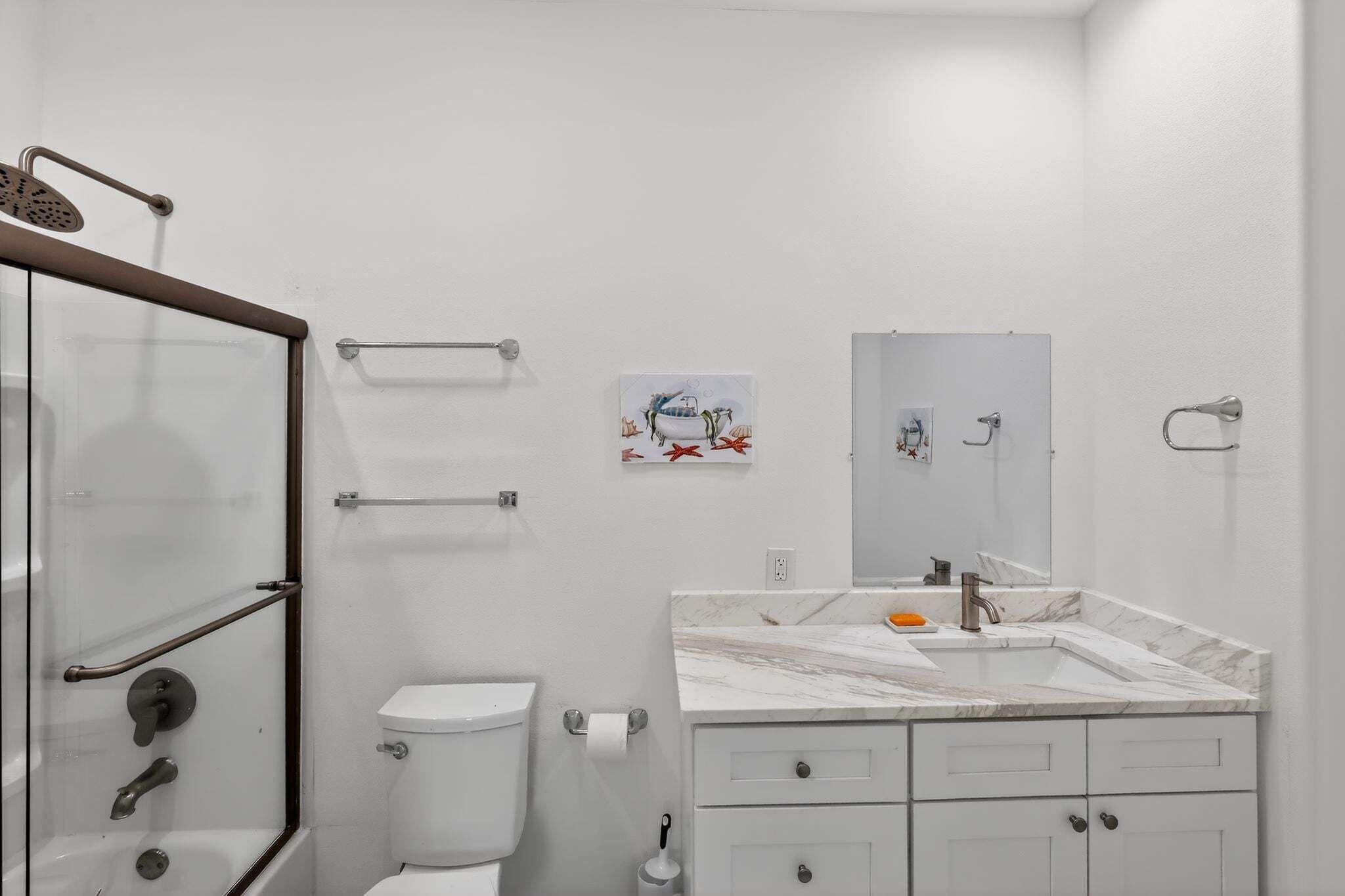 A modern bathroom with a glass shower enclosure, a white toilet, a marble sink, and a small artwork on the wall.