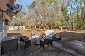 Une terrasse extérieure avec une table et des chaises abritées, un ventilateur et un espace barbecue couvert.
