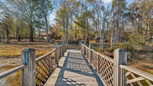 A wooden boardwalk leading through a wooded area with trees and a building in the background. - Healing Adventures Wellness Retreat 3 Bedroom Home (Claxton)