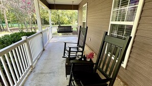 A covered porch with two rocking chairs, a bench, and a small table with a vase of flowers. - Healing Adventures Wellness Retreat 3 Bedroom Home (Claxton)