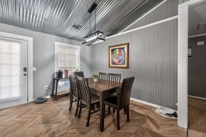 Un coin repas avec une table et des chaises en bois, un ventilateur de plafond et un tableau accroché au mur.