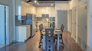 Une cuisine moderne équipée d’appareils électroménagers en acier inoxydable, une table à manger pour quatre personnes et une vue sur le salon attenant.