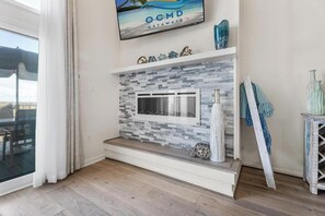 Ein modernes Wohnzimmer mit Kamin, einem darüber hängenden Fernseher und Blick ins Freie durch ein großes Fenster.
