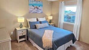 Een slaapkamer met een bed, twee nachtkastjes met lampen, een plafondventilator, een raam met gordijnen en een schilderij aan de muur.