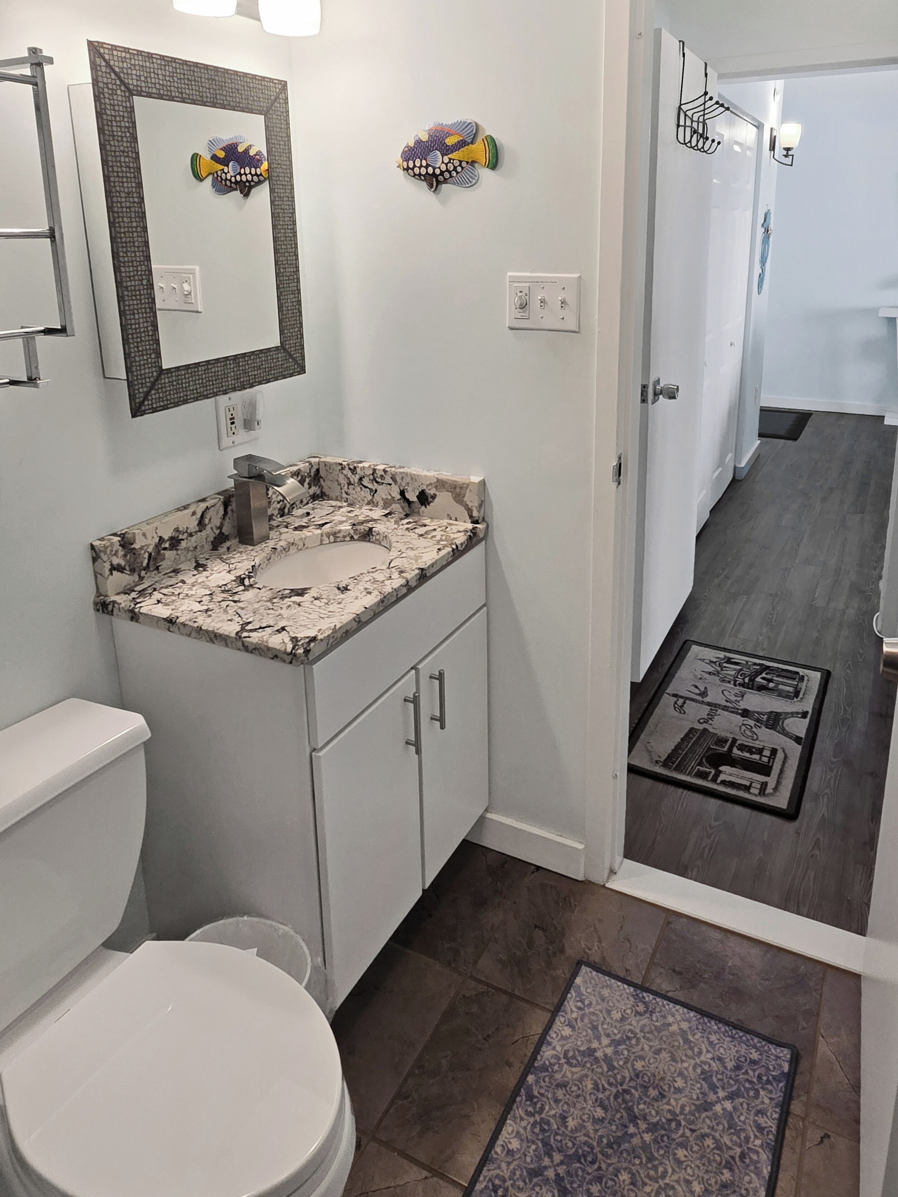 A bathroom with a white toilet, a marble sink, a mirror, and a fish wall art piece.