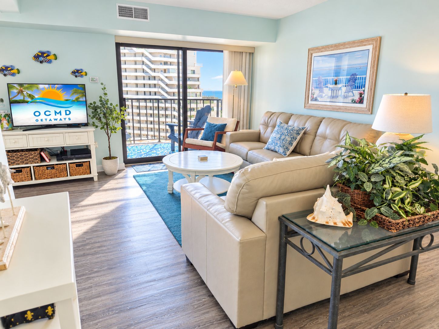 A hotel room with a balcony, a television, a sofa, a coffee table, and a dining table with plants.