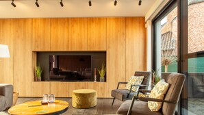 Una sala de estar moderna con una pared de madera, un televisor de pantalla plana, una mesa de centro redonda y asientos cómodos.