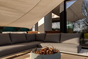 Uma área de estar moderna ao ar livre, com um sofá modular grande e uma cesta trançada em primeiro plano.