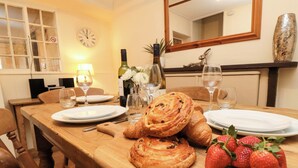 A dining table set with plates, cutlery, wine glasses, a bottle, and pastries. - Beacon Cottage (Pickering)