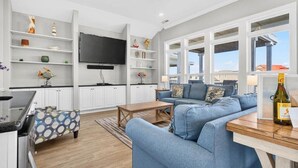 A modern living room with a blue sofa, wooden coffee table, and a flat-screen TV. There are white cabinets and shelves with decorative items. - Sea Esta is a 7-bedroom, 5-bathroom, large enough for the whole family! (Ocean Isle Beach)