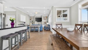 A spacious kitchen with a wooden dining table and bar stools, a built-in oven, and a large window providing natural light. - Sea Esta is a 7-bedroom, 5-bathroom, large enough for the whole family! (Ocean Isle Beach)