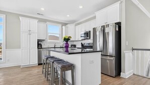 A modern kitchen with white cabinetry, stainless steel appliances, and a central island with bar stools. - Sea Esta is a 7-bedroom, 5-bathroom, large enough for the whole family! (Ocean Isle Beach)