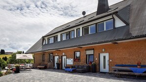 A building with a brick exterior, a covered patio area with outdoor seating, and a door marked with a 'P' for parking. - Holiday Home 'Sport Rees - 7 Fewo Eventraum' with Mountain View, Private Terrace & Wi-Fi (Oberried)
