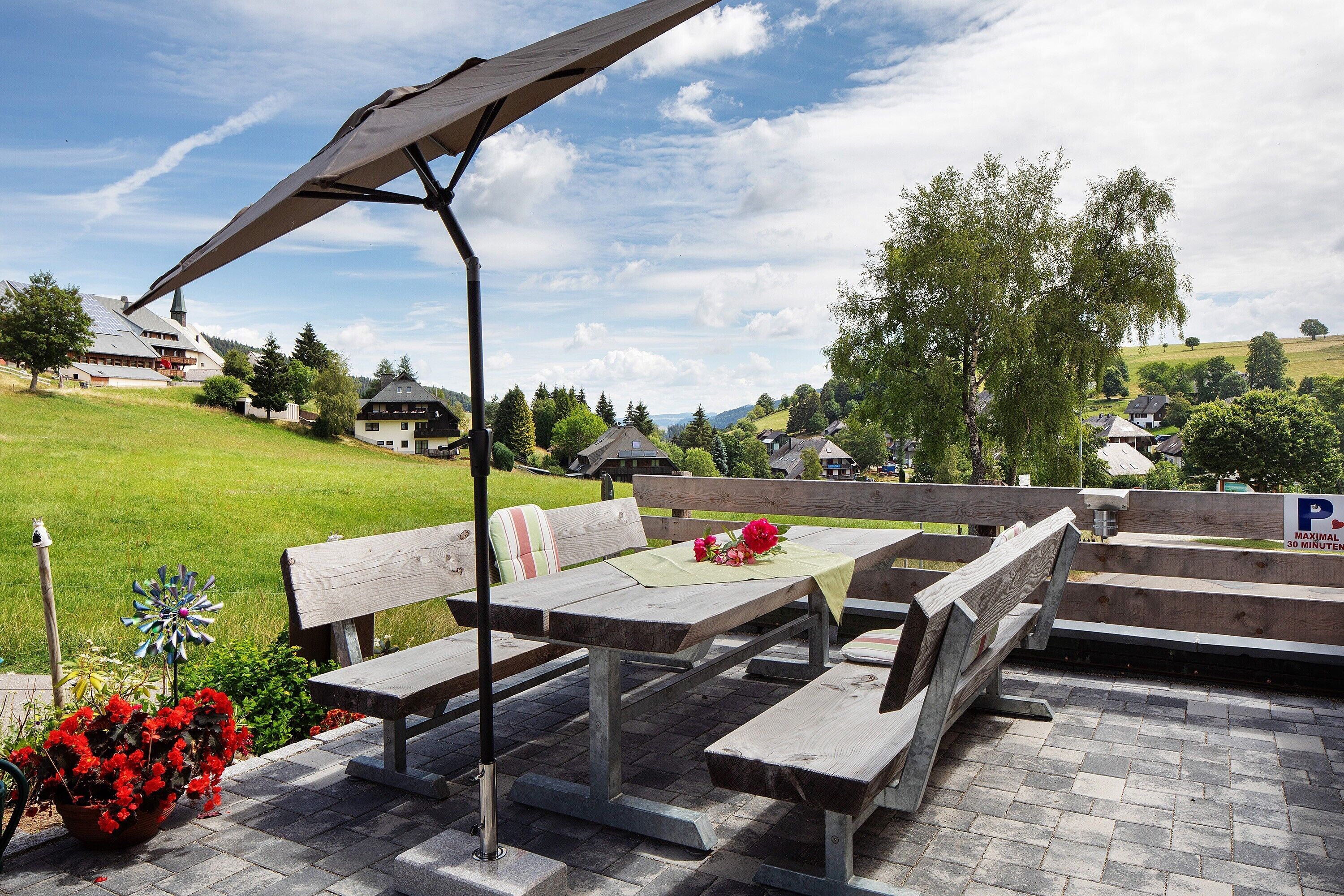 An outdoor seating area with picnic tables and benches, a metal umbrella, and a flower arrangement.